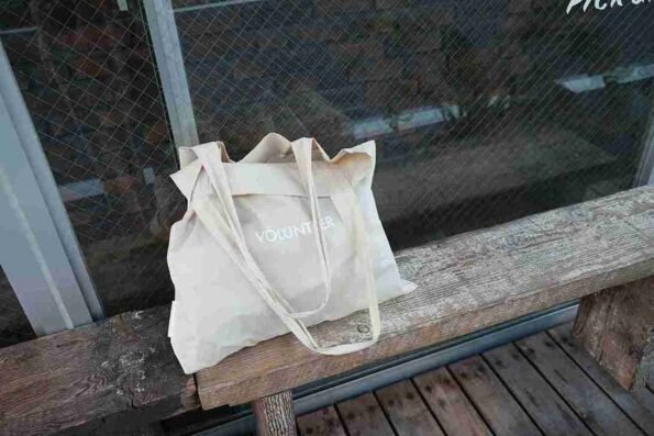 Totebag custom volunteer warna krem di atas bangku kayu, cocok untuk kegiatan sosial atau branding komunitas.